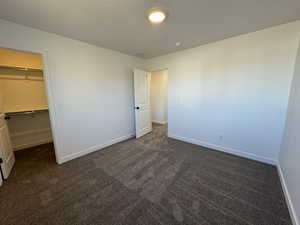 Unfurnished bedroom with dark carpet and a walk in closet