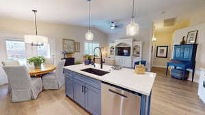 Kitchen featuring stainless steel dishwasher, light stone counters, a kitchen island with sink, light wood finished floors, and lofted ceiling
