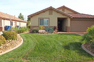Mediterranean / spanish house featuring stone siding, stucco siding, a front lawn, a tile roof, and a garage