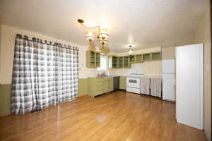 Kitchen with green cabinets, white appliances, a textured ceiling, light wood-style flooring, and pendant lighting