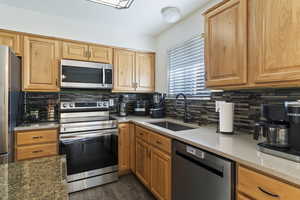 Kitchen with appliances with stainless steel finishes, tasteful backsplash, light stone counters, and dark wood-type flooring