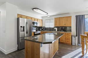 Kitchen featuring stainless steel appliances, a kitchen island, dark wood finished floors, backsplash, and dark stone counters