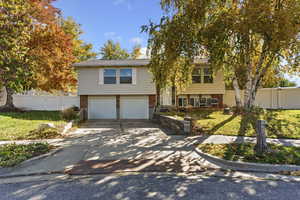 Raised ranch with brick siding, concrete driveway, and an attached garage