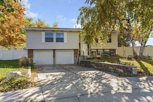 Raised ranch featuring brick siding, concrete driveway, an attached garage, and a gate