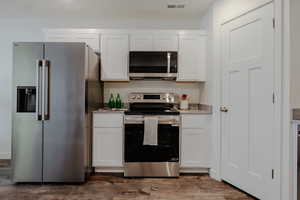 Kitchen featuring stainless steel appliances, white cabinets, light stone counters, and dark wood-type flooring