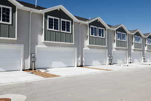 View of front of home with board and batten siding, concrete driveway, stucco siding, a residential view, and an attached garage