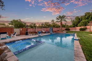 Pool at dusk with a fenced backyard, a water slide, a patio, a diving board, and a pool with connected hot tub