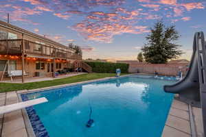 View of swimming pool featuring a patio area, a water slide, stairs, a diving board, and a wooden deck