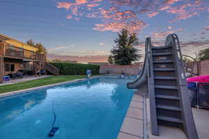 View of pool with stairway, a patio area, a water slide, a fenced backyard, and a wooden deck