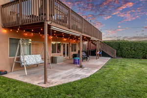 Back of property at dusk featuring a patio area, stairs, a lawn, stucco siding, and a wooden deck