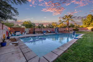 Pool at dusk with a water slide, a fenced backyard, a patio, and a pool with connected hot tub
