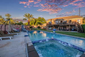 Pool at dusk with a patio area, stairs, a water slide, a wooden deck, and a pool with connected hot tub