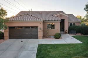View of front of home with an attached garage, driveway, stucco siding, a tiled roof, and a front yard
