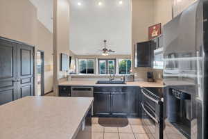 Kitchen with stainless steel appliances, light countertops, light tile patterned floors, high vaulted ceiling, and a ceiling fan