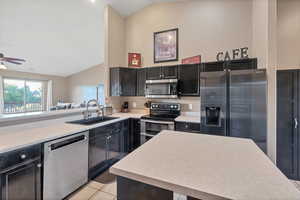 Kitchen with stainless steel appliances, light countertops, light tile patterned floors, dark cabinets, and high vaulted ceiling