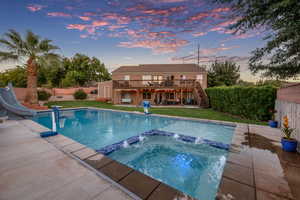Pool at dusk featuring a patio area, stairs, a deck, a water slide, and a pool with connected hot tub