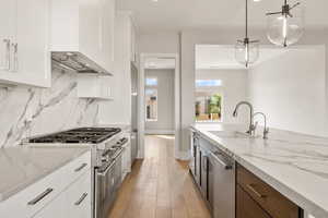 Kitchen featuring premium appliances, white cabinetry, custom range hood, hanging light fixtures, and light stone countertops