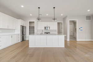 Kitchen with white cabinets, recessed lighting, stainless steel appliances, hanging light fixtures, and light wood-type flooring