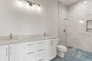 Full bath with double vanity and a marble finish shower