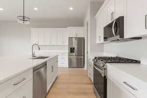 Kitchen featuring appliances with stainless steel finishes, white cabinets, recessed lighting, light wood-style floors, and hanging light fixtures