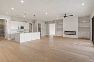 Kitchen featuring white cabinetry, light wood-type flooring, decorative light fixtures, recessed lighting, and a center island with sink