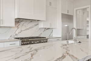 Kitchen featuring white cabinetry, light stone counters, decorative backsplash, and custom exhaust hood