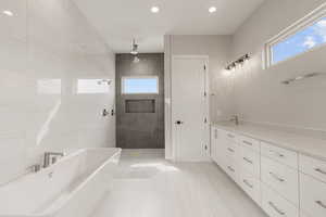 Full bath featuring a freestanding bath, vanity, light tile patterned floors, recessed lighting, and tile walls