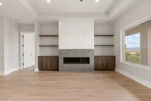 Unfurnished living room with a fireplace, a tray ceiling, recessed lighting, and light wood-type flooring