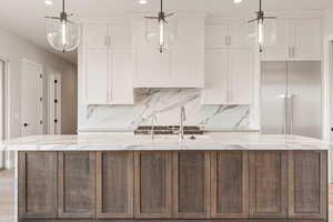 Kitchen featuring light wood finished floors, light stone counters, recessed lighting, a kitchen island with sink, and white cabinetry