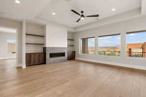 Unfurnished living room with a raised ceiling, light wood-style flooring, ceiling fan, a high end fireplace, and recessed lighting