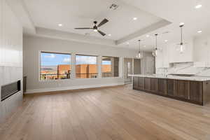 Unfurnished living room featuring a tray ceiling, light wood-style floors, a ceiling fan, recessed lighting, and a glass covered fireplace