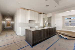 Kitchen featuring dark brown cabinetry, white cabinetry, a center island, baseboards, and visible vents
