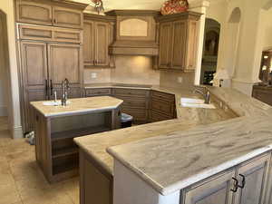 Kitchen with backsplash, light stone counters, premium range hood, and a peninsula