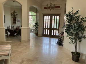 Elegant Front Door Entrance, Foyer with a chandelier, french doors, ornamental molding, arched walkways, and light tile patterned floors