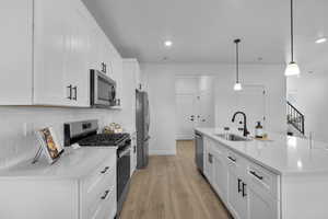 Kitchen featuring appliances with stainless steel finishes, white cabinetry, light stone counters, an island with sink, and recessed lighting