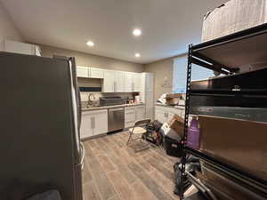 Kitchen featuring appliances with stainless steel finishes, backsplash, white cabinetry, wood tiled floors, and recessed lighting