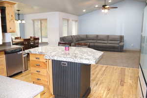 Kitchen with light brown cabinetry, dishwasher, open floor plan, vaulted ceiling, and decorative light fixtures