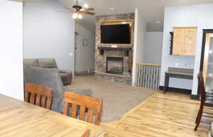 Living area with ceiling fan, a stone fireplace, light wood-type flooring, and lofted ceiling