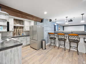 Kitchen featuring dark countertops, tasteful backsplash, light wood-type flooring, freestanding refrigerator, and white cabinetry