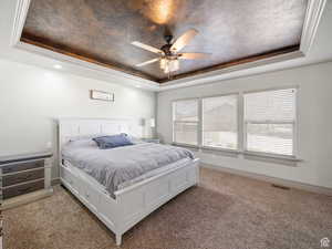 Bedroom with visible vents, a tray ceiling, ceiling fan, and light colored carpet
