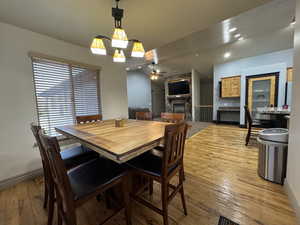 Dining room with a fireplace, light wood finished floors, a chandelier, a ceiling fan, and recessed lighting