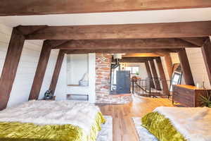 Bedroom with light wood-style flooring, beam ceiling, and wooden walls