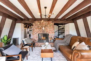 Living room featuring a large fireplace, wood walls, stairs, a chandelier, and beam ceiling