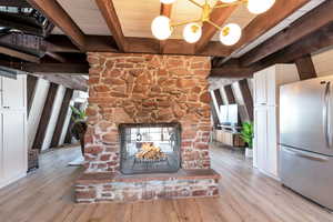 Detailed view of freestanding refrigerator, white cabinetry, a fireplace, light wood-style flooring, and a wood ceiling with exposed beams