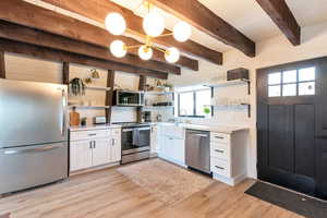 Kitchen with white cabinets, appliances with stainless steel finishes, decorative backsplash, open shelves, and light wood-type flooring