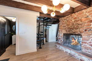 Unfurnished living room featuring stairway, a stone fireplace, wood finished floors, and beamed ceiling