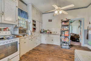 Kitchen with white range oven, dark wood-style flooring, light countertops, and ceiling fan
