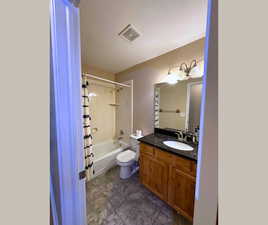 Bathroom featuring tub / shower combination, vanity, and dark tile patterned floors