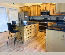 Kitchen featuring appliances with stainless steel finishes, dark stone countertops, a breakfast bar area, light wood-style floors, and a kitchen island