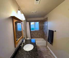 Bathroom featuring vanity, shower / bathtub combination with curtain, and a textured ceiling